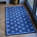Blue doormat with white and yellow floral patterns on a wooden floor. It is placed near glass doors, enhancing a cosy, welcoming feel.