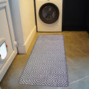 Laundry room with a black and white diamond-patterned rug on a stone tile floor, placed in front of a white washing machine with a circular door.