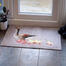 A charming doormat with a painted goose leading three ducklings is placed by a glass door. A potted plant and black boots are nearby on the wooden floor.