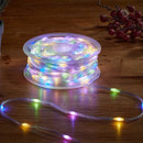 Coiled reel of clear string lights on a wooden table, lit in multicolour (blue, green, purple, and yellow), with a short section of lights unspooled in front and decorative red berries in the background.