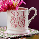 White half-pint mug with pink ‘Soul Sisters & Best Friends’ lettering, styled with a pink dahlia on a patterned cloth.