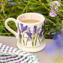 Emma Bridgewater blue iris half-pint mug filled with tea, styled outdoors among garden flowers.