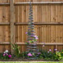 Tall slate-colour faux rattan garden obelisk supporting climbing flowers in a flower bed against a wooden fence.