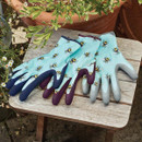 Three pairs of blue bee-print gardening gloves with textured grip fingers laid on a wooden garden table.