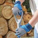 Hands wearing blue and grey protective work gloves gripping the handle of a shovel in front of stacked logs.