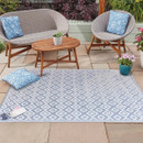 Light blue and white diamond-pattern outdoor rug on a patio, styled with wicker lounge seating, a wooden coffee table, and blue cushions.