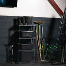 A tidy garage with black storage shelves holding bins, a bucket, and boots. Nearby are a bicycle, broom, and tools, conveying a sense of organized space.