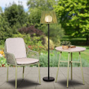 Sage green outdoor floor lamp with a slatted shade on a black stand, styled beside a patio chair and table in a garden setting.
