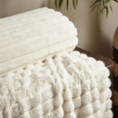 Close-up of a cream faux fur throw showing soft ribbed and bubble textures.