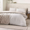Beige and white pinstripe duvet cover styled with a soft throw, creating a relaxed and minimalist bedroom look.