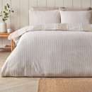 Reversible beige striped bedding set on a bed, showing a lighter striped reverse with matching pillowcases in a neutral interior.