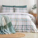 Green tartan bedding set styled with coordinating pillowcases and a folded green throw at the foot of the bed.