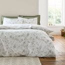 White duvet cover with soft green floral pattern styled in a bright bedroom with wooden floor and window light.