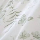 Macro close-up of white bedding fabric showing soft green leaves and butterfly print with smooth cotton texture.