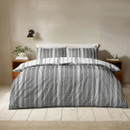 Reversible striped duvet cover showing the darker grey side, styled on a neatly made bed in a minimalist bedroom.