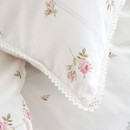 Detailed close-up of a pillowcase corner showing pink floral motif and scalloped lace edging.