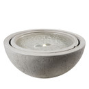 A textured grey concrete bowl fountain with gently rippling water, softly illuminated by a central light. The design exudes calm and elegance.