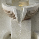 Close-up of water flowing from a sculpted spout into a ridged bowl on the fountain.