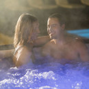 Couple relaxing together in a Lay-Z-Spa Maldives inflatable hot tub at night with illuminated water and steam.