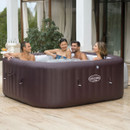 Group of friends enjoying a brown Lay-Z-Spa Maldives inflatable hot tub on a sunlit patio outside a modern home.