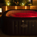 Lay-Z-Spa Maldives inflatable hot tub illuminated with red LED lighting in a landscaped garden at night.