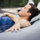 Man reclining comfortably in an inflatable hot tub using a padded headrest, eyes closed in relaxation.