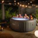 Group of people relaxing together in a Lay-Z-Spa inflatable hot tub outdoors at night with ambient garden lighting.