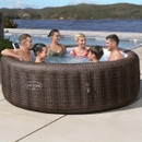 Group of six adults socialising in a rattan-effect Lay-Z-Spa inflatable hot tub with a sea view in the background.