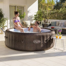 A couple enjoying a Lay-Z-Spa rattan-effect inflatable hot tub beside a small outdoor table with drinks.