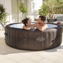 Two adults relaxing and talking in a brown rattan-style Lay-Z-Spa inflatable hot tub on a sunny patio.