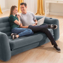 Couple sitting on a grey inflatable sofa bed using a laptop in a bright living room.