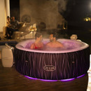 Couple relaxing in a Lay-Z-Spa Hollywood inflatable hot tub with purple LED lighting at night on a patio.