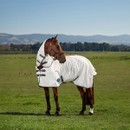 Side view of a horse wearing a white turnout rug with integrated neck cover, standing on green pasture with rolling hills in the background.
