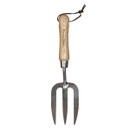 Wooden-handled garden fork with three sharp metal prongs, featuring a leather loop at the top. The tool conveys a rustic, practical tone.