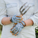 A person in a light denim shirt holds a garden fork, wearing blue floral-patterned gloves. The scene conveys a calm, gardening-focused mood.