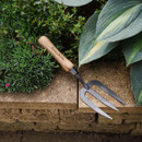 Wooden-handled garden fork resting on a stone ledge surrounded by lush green foliage and hosta leaves, conveying a serene gardening scene.