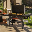 Blackstone 4-burner gas griddle with hood cooking vegetables and chicken on an outdoor patio.