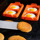 Pancakes cooking on a griddle beside Blackstone orange two-section egg ring moulds with fried eggs