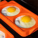 Close-up of fried eggs cooking inside a Blackstone orange two-section egg ring mould on a griddle