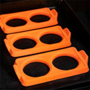 Three Blackstone orange two-section silicone egg ring moulds placed on a flat top griddle