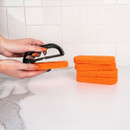 Hand attaching an orange scouring pad to a Blackstone scrub pad handle on a kitchen worktop.
