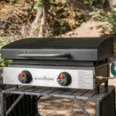 Blackstone portable gas griddle with hood closed on outdoor stand, stainless steel control panel and dual burner knobs for camping or garden cooking.