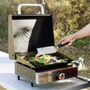 Blackstone single burner tabletop gas griddle with hood open, cooking vegetables on a flat top surface in an outdoor setting.