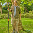 Man in casual clothing stands by tree in lush garden, confidently holding an orange and black garden tool. Sunlight filters through the green leaves.