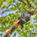 Telescopic pruner cutting a tree branch, surrounded by lush green leaves against a clear blue sky. The tool appears sturdy and efficient.