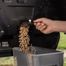 Wood pellet hopper clean-out chute on Traeger grill releasing pellets into a storage container below.