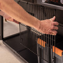 Traeger Woodridge Pro lower cabinet with metal storage basket panel being attached by hand, pellet bins visible behind.