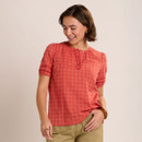 Woman wearing a coral short-sleeved blouse with a small red and white scattered print, round neckline and button placket detail.