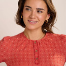 Close-up of the coral printed blouse showing the round neckline, decorative stitched placket with buttons, and delicate gathered detail at the shoulders.