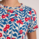 Close-up of a cream T-shirt with blue leaf and red floral print, featuring ladder trim detailing at the neckline and sleeves.